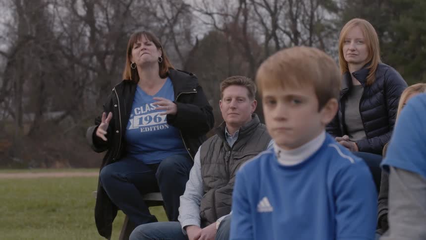Parents in the stand yell as a boy sits on the bench