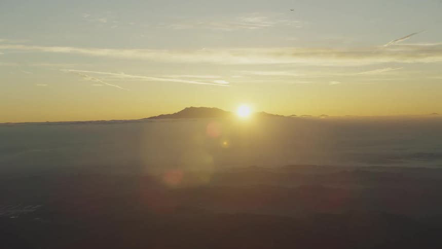 The sun is slowly setting behind the mountain; aerial zoom out