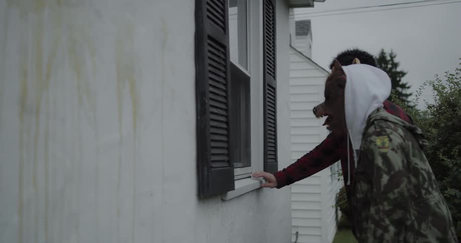 Two people in halloween masks peek in a homes window