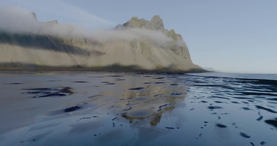 The beach is wet with a white mountain at the end