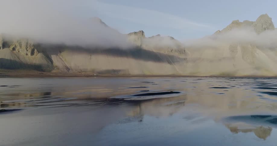 Clouds are hanging below the tops of hills on a remote coastline in daylight