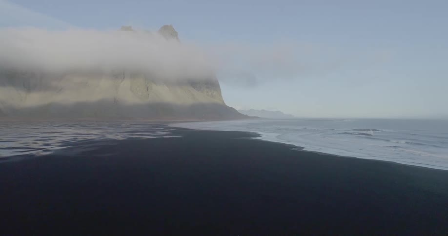 The ocean is washing up on a black beach