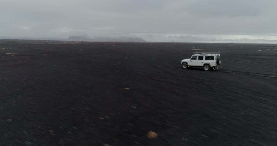 A jeep is driving across a black dirt covered landscape