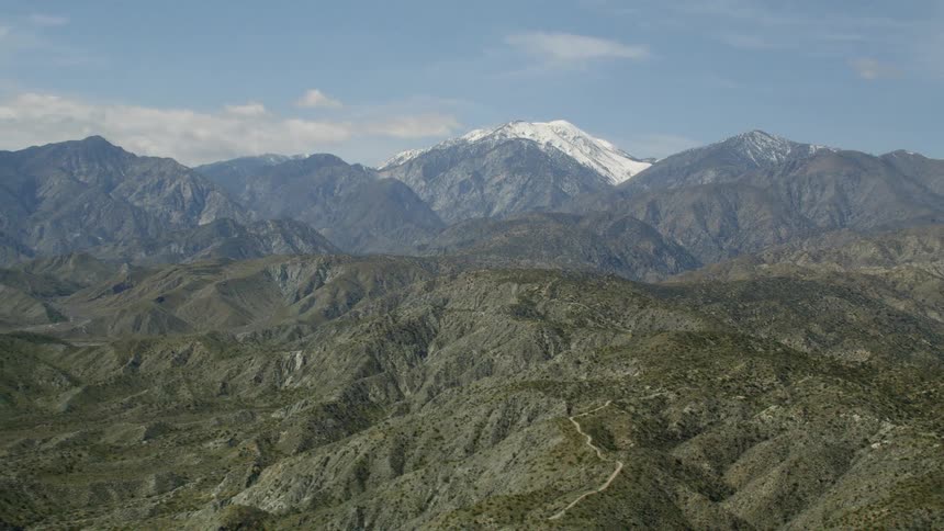The hills are green leading up to the snow covered tall mountain