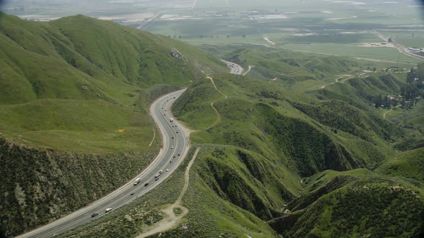 Cars travel on a road over green hills