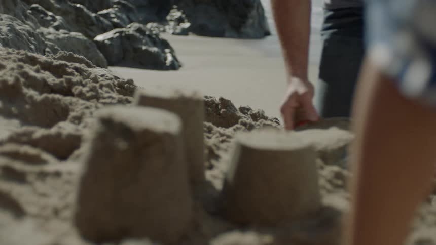 Father and son building sand castle on sand next to the ocean