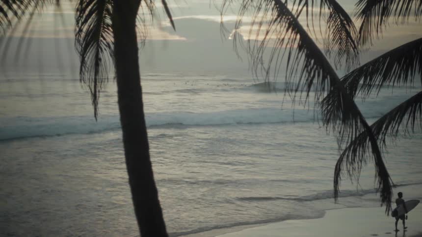 Person carrying a surfboard walks on the beach at sunset