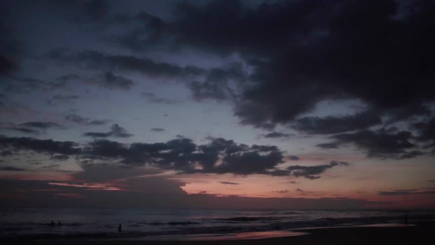 People wade in the shallow beach water at dusk