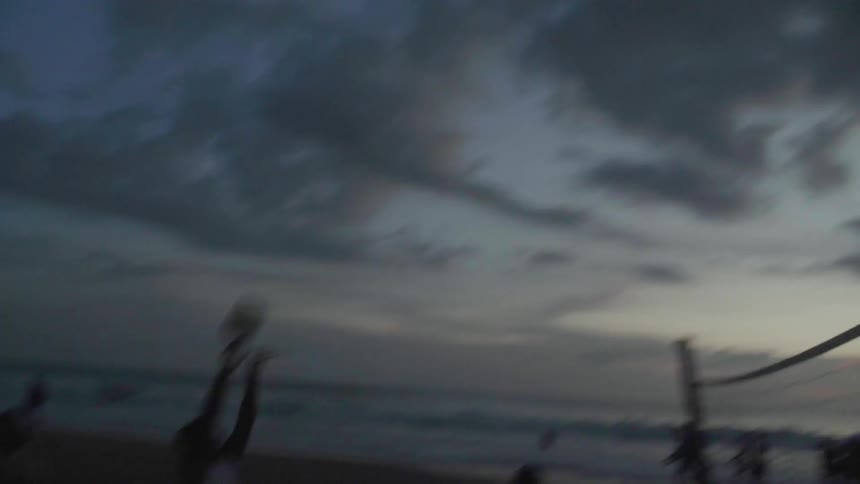 People play volleyball on a beach at sunset