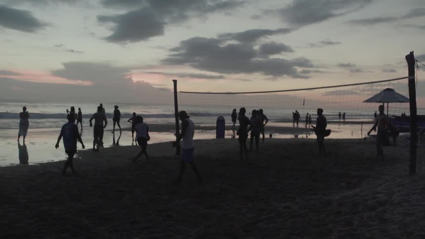 Group of people playing beach volleyball near a cloudy sunset