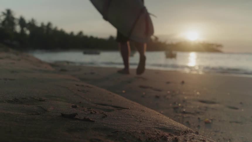 Person picks up a surfboard and walks down the beach