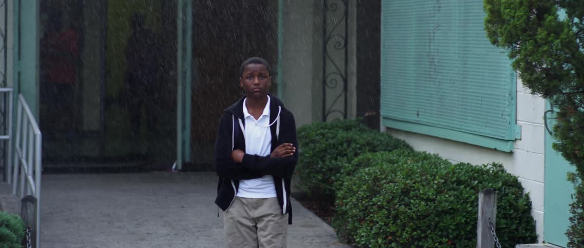 Child stands outside of a building and it starts to rain