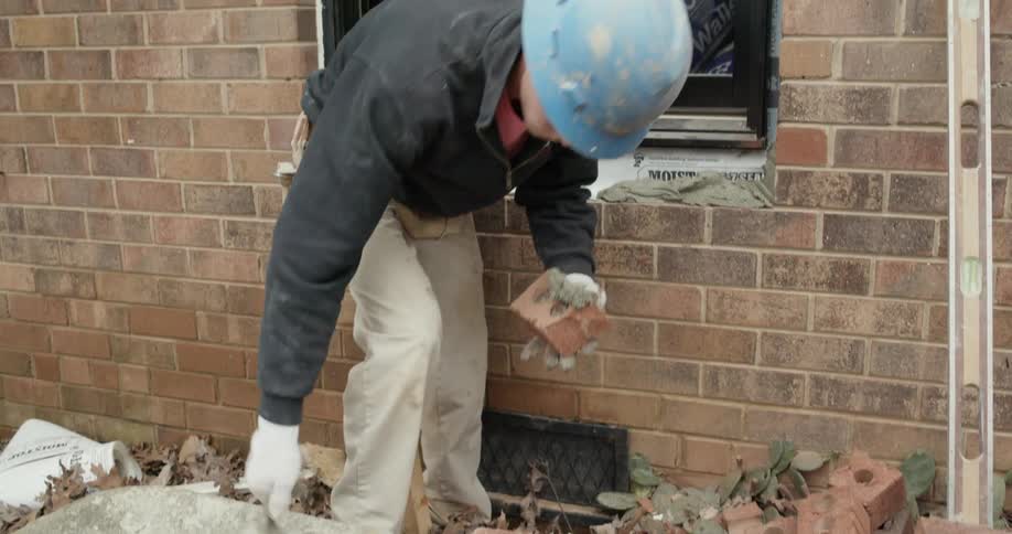 A construction worker lays brick on a windowsill