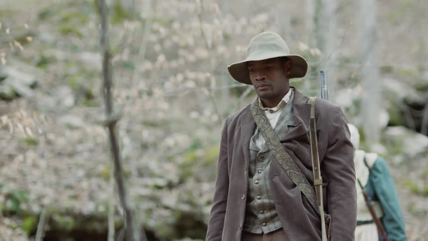 A man stands up and puts on his hat in the woods