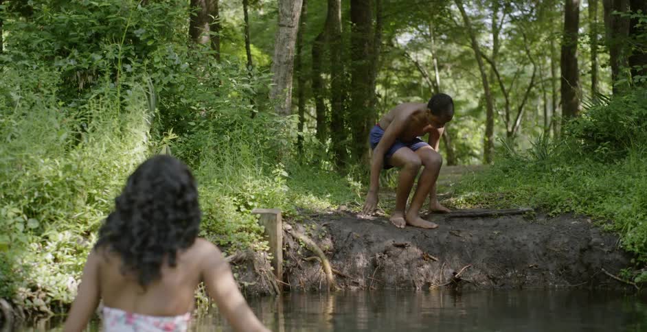 A woman encourages a boy to get into a lake