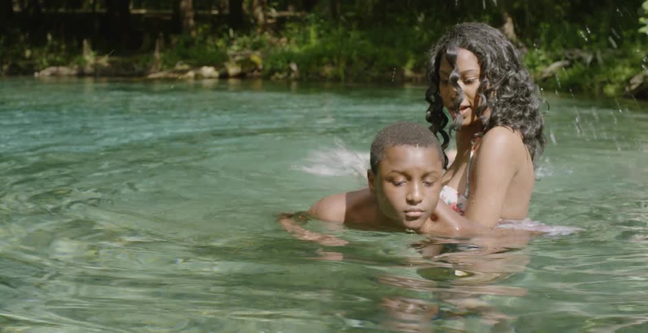 A woman helps a young boy swim in a river