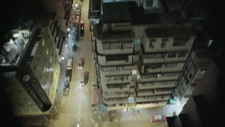 A man stands on a rooftop overlooking a city at night