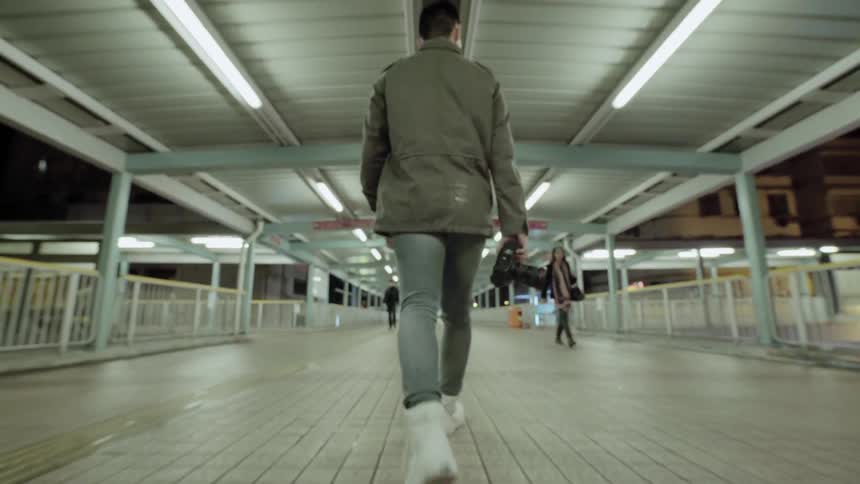 A man carries a camera as he walks across a bridge