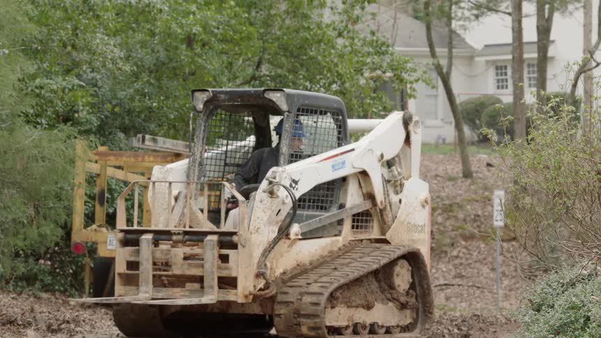 The man is driving a construction vehicle backwards