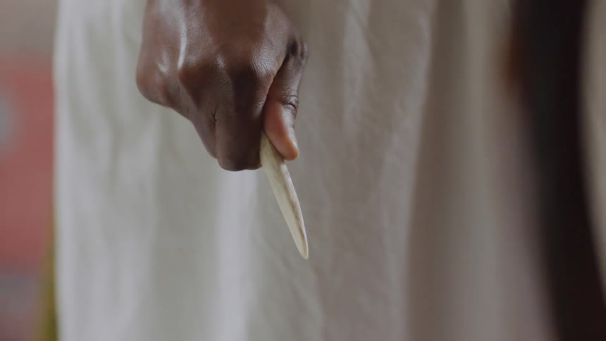 A woman holds a sharpened piece of wood tightly