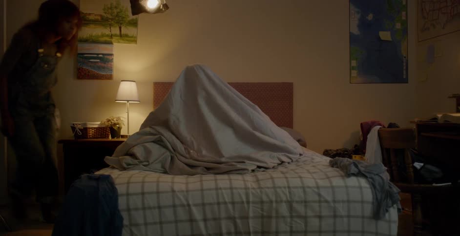 A young child plays under a bed sheet on a bed