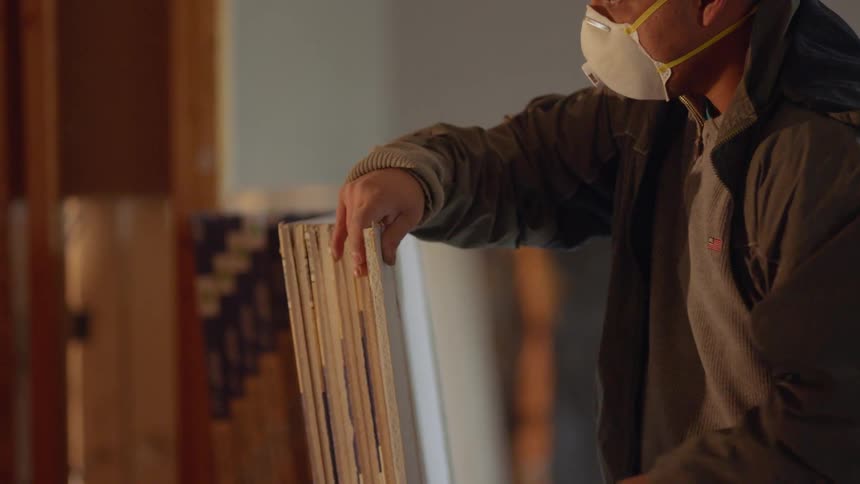 Man wearing a mask cuts drywall with a pocket knife