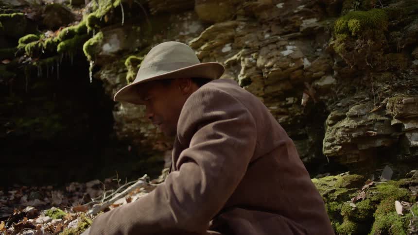 A man is searching through a pile of rocks in a natural setting in daylight