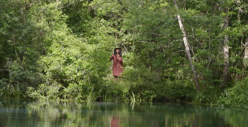A woman walks towards a river through the woods