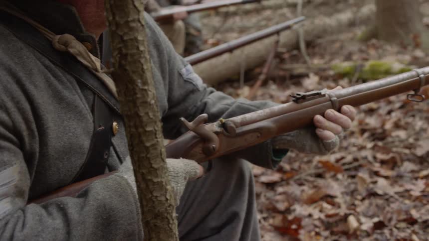 A line of soldiers aim their rifles in the woods