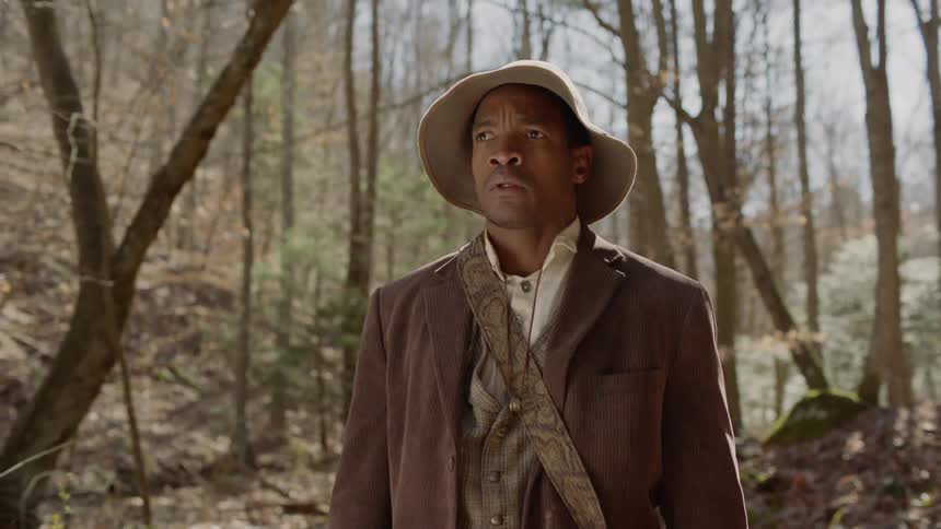 A black man from the 1800s is dropping a rifle as he stands outside in daylight