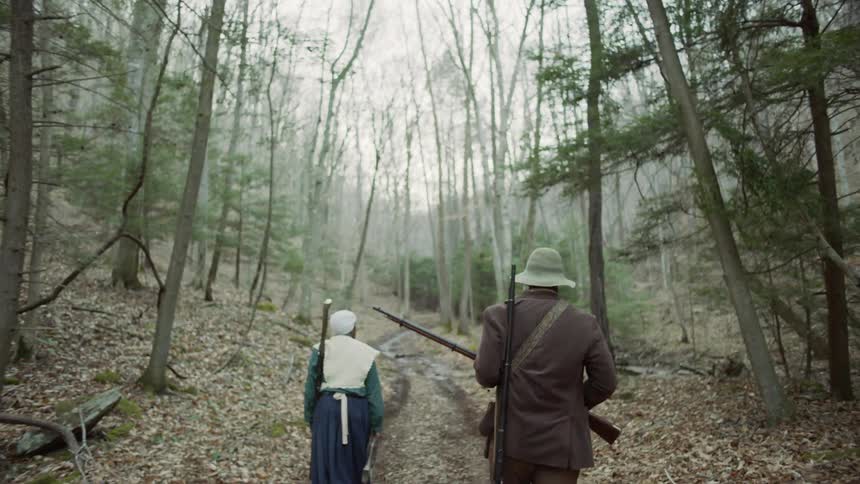 Man and woman walk in a forest with rifles