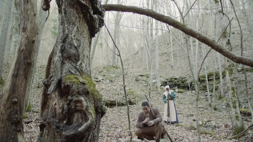 A man and woman carry rifles in a forest