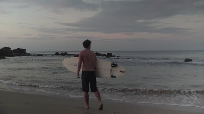 A man carries his surfboard past the shore
