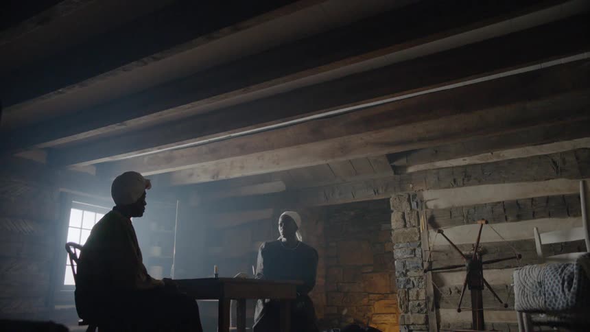 Two women sit at a wooden table in a dim room