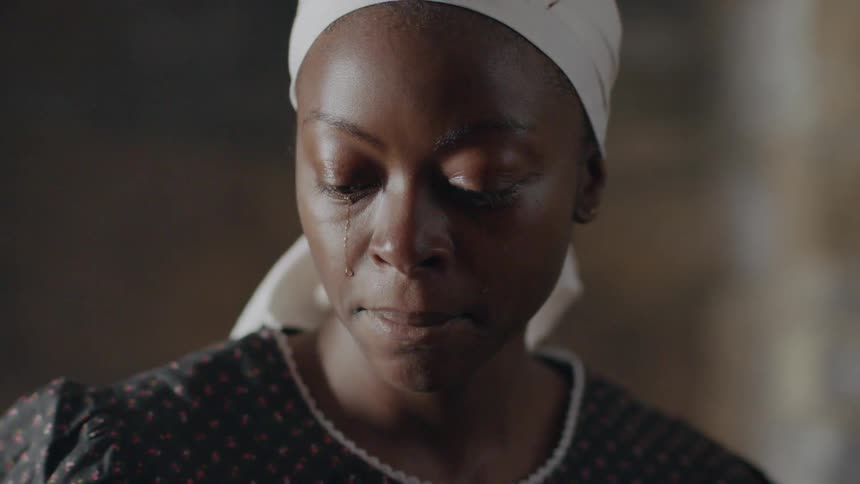 A slave woman is smiling and crying as she stands inside in daylight