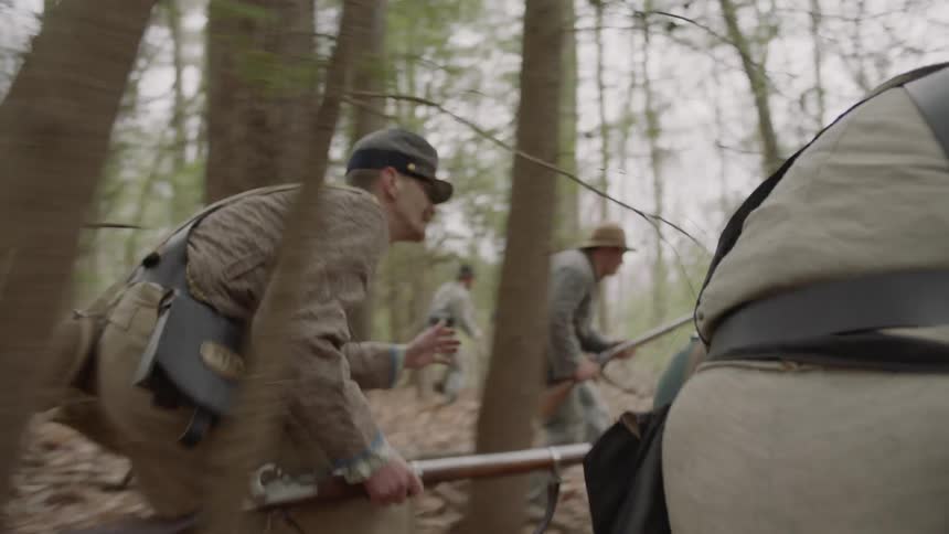 Confederate soldiers are running through a forest hunting the opposition in daylight