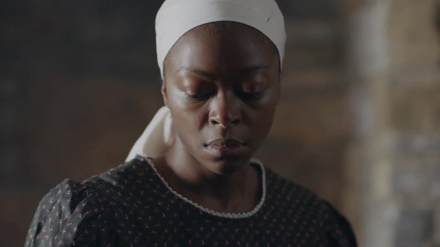 A woman in servant garb stares forward