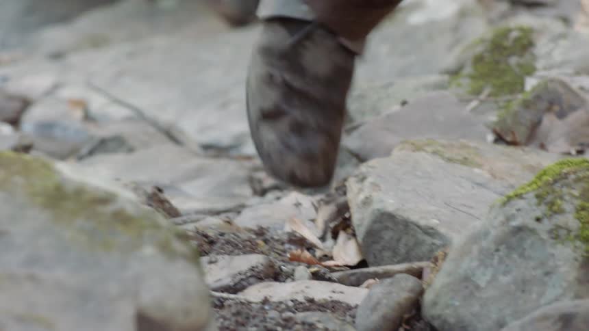 Men wearing boots make their way over rocks and stones