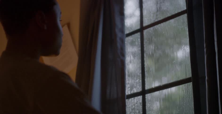 Child looks outside at the rain and closes the curtains to the window