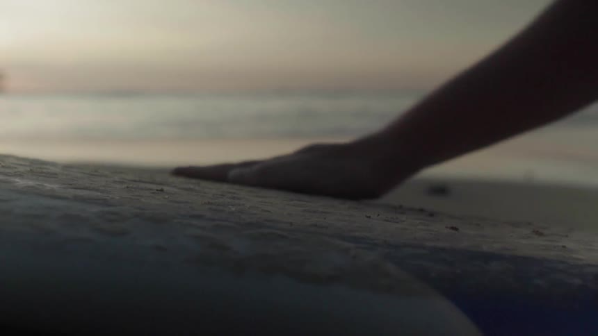 A surfer rubs the sand off his surfboard at sunset