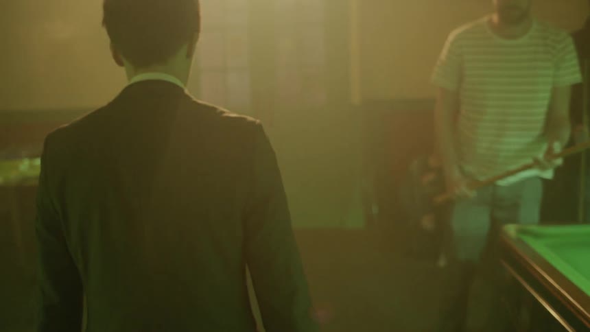 A man is walking through a pool hall and into a hallway at night