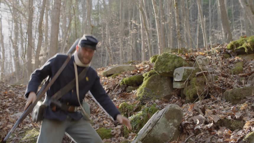 A soldier carrying a rifle walks through the woods