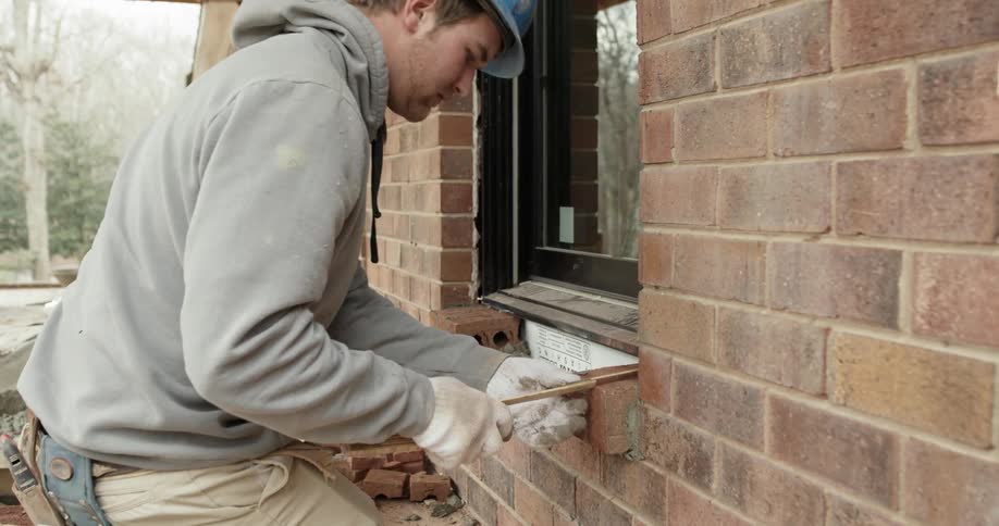 A construction worker places brick on a window ledge