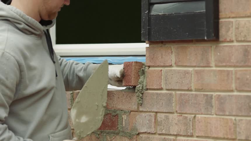 A construction worker lays brick on a windowsill