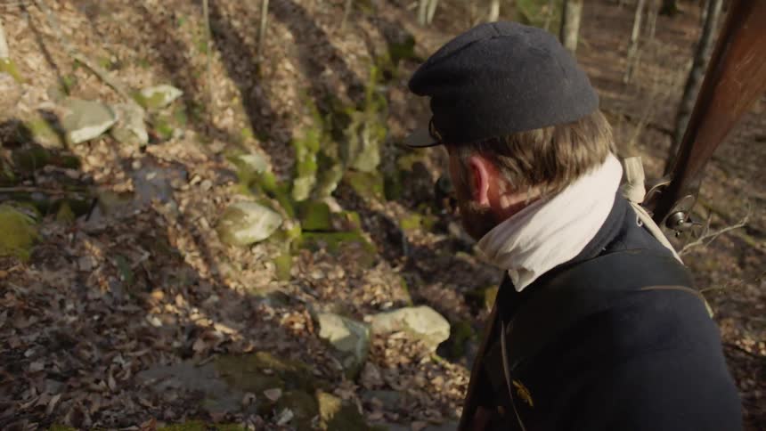 A 19th century soldier stands in a forest with a rifle