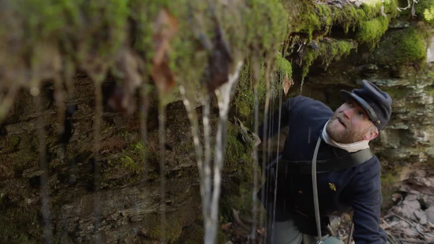 A man crawls out from under a wet cave