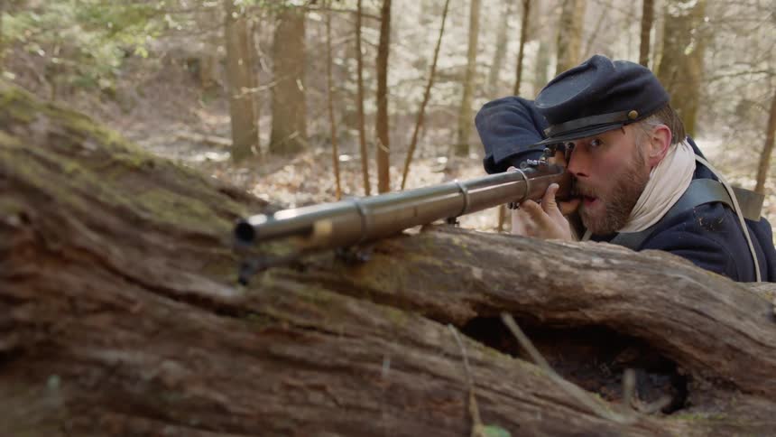 A 19th century soldier aims a rifle over a fallen tree