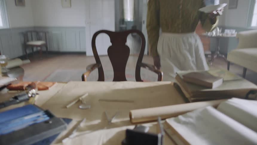 A slave woman is hurriedly taking a piece of paper from a desk inside in daylight