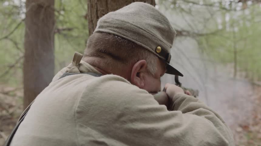 Man aims his rifle and shoots in the woods
