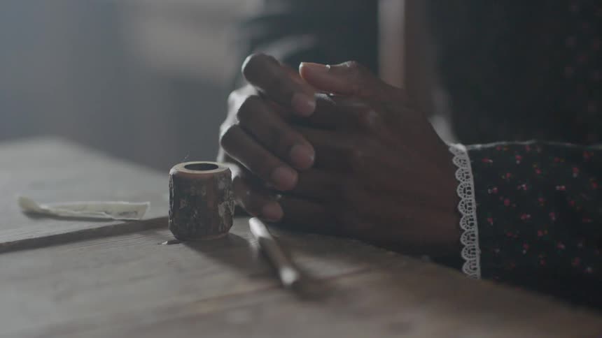 A woman is sitting inside at a table clutching her hands